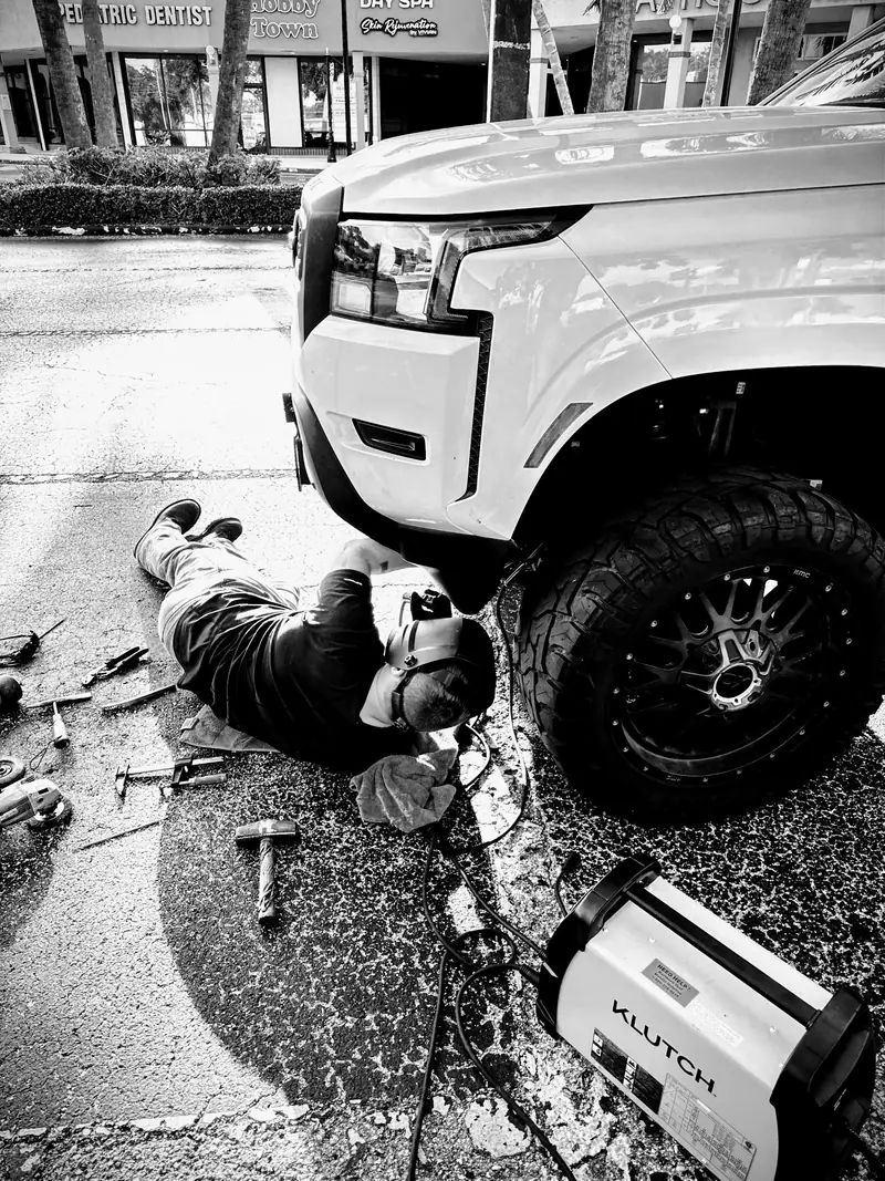 On-site welding under a pickup truck with a portable welder on the pavement